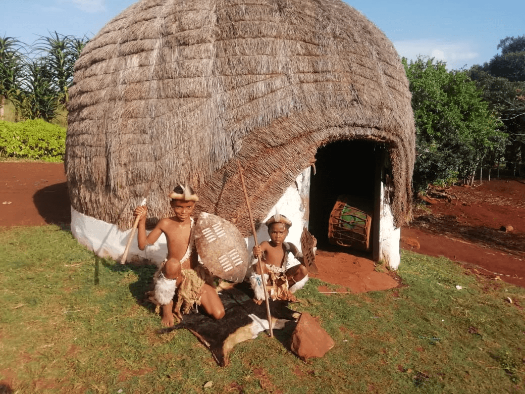 Zulu cultural guide beside a traditional hut at Mzamo's Cultural Village & Homestead